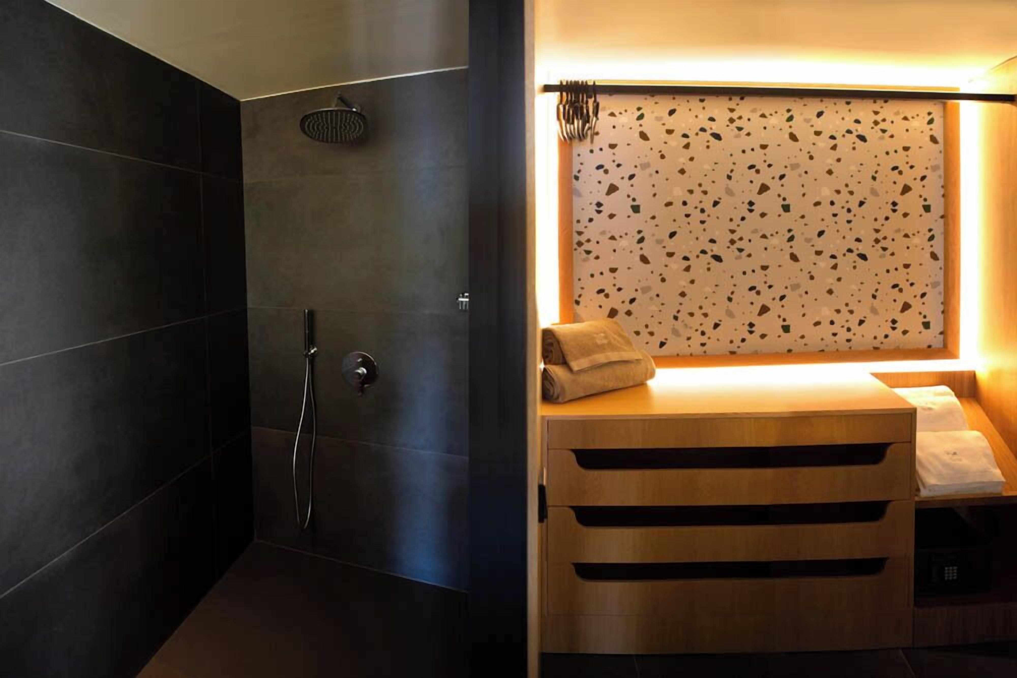 A modern bathroom with dark tiles, a shower, and a wooden vanity with a towel.