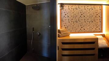 A modern bathroom with dark tiles, a shower, and a wooden vanity with a towel.