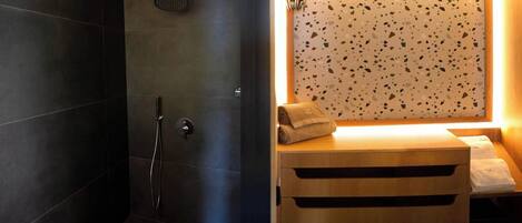 A modern bathroom with dark tiles, a shower, and a wooden vanity with a towel.