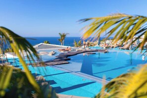 A clear blue infinity pool with lounge chairs and palm trees, overlooking the ocean.
