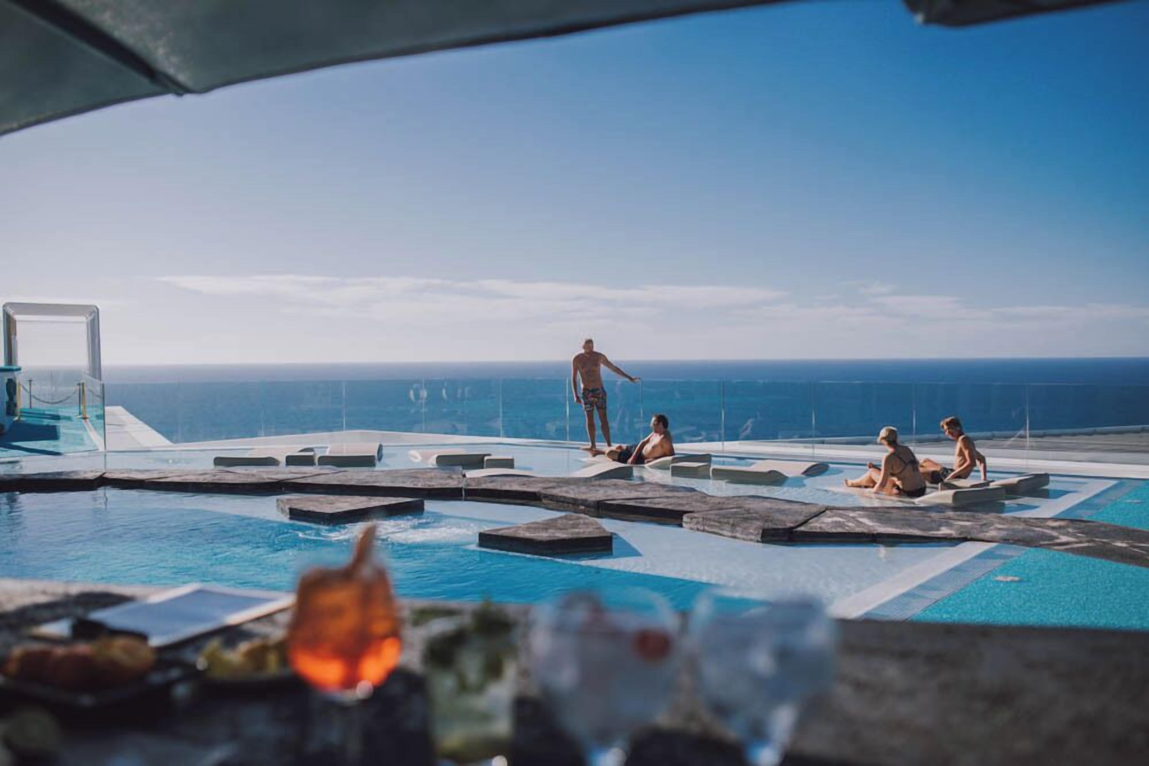 Un área de piscina con vista al océano, que incluye una silla de descanso y una mesita con una bebida.