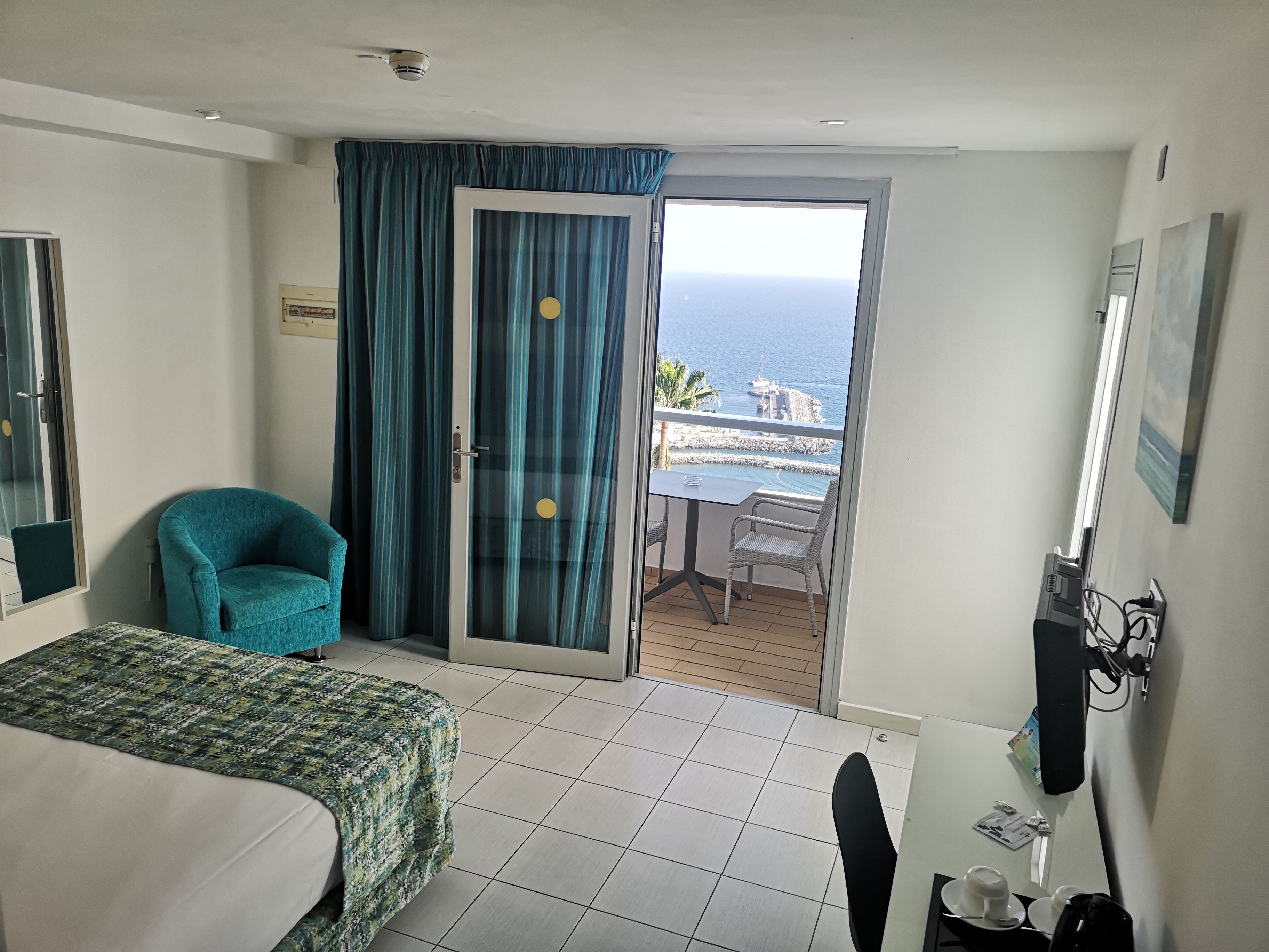 Ett hotellrum med en säng, en stol, ett bord och utsikt över havet genom en skjutdörr.