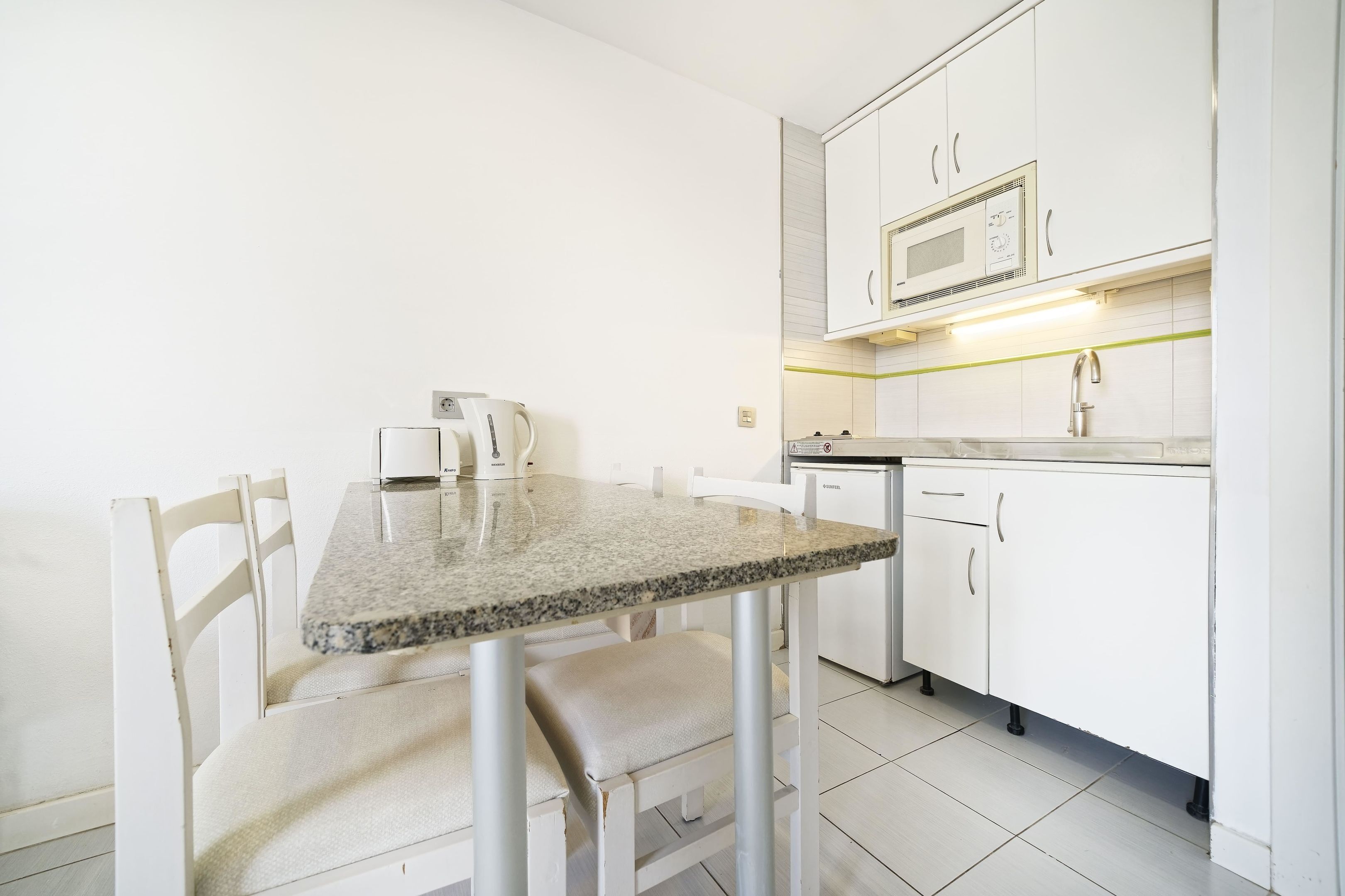 A compact kitchen with white cabinets, a granite countertop, and a microwave.