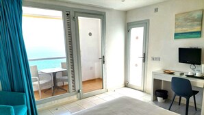 Et hotelværelse med seng, skrivebord med computer, stol og tv. Der er en balkon med havudsigt.