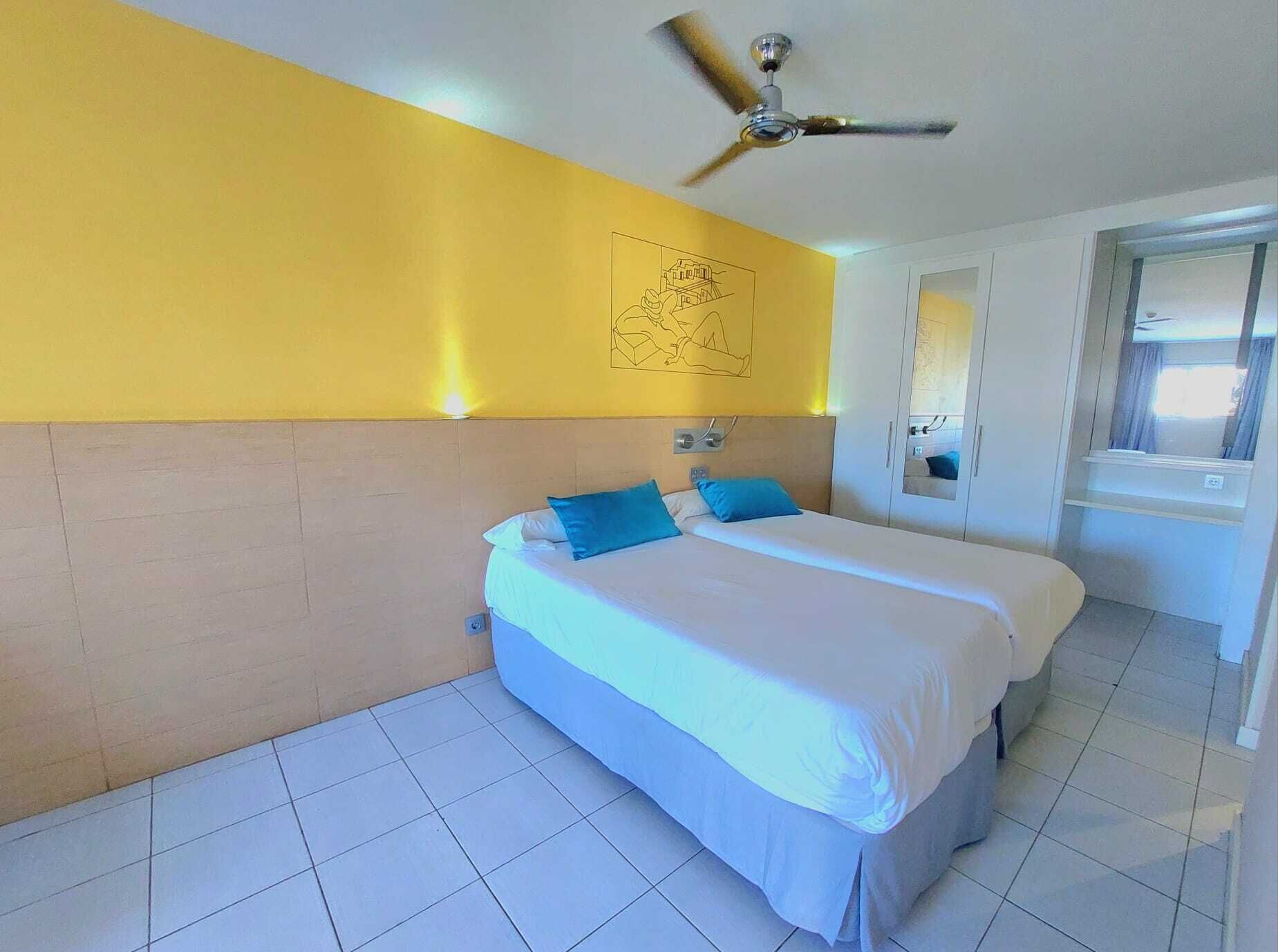 Een hotelkamer met een bed, een plafondventilator en een muur met een muurschildering.