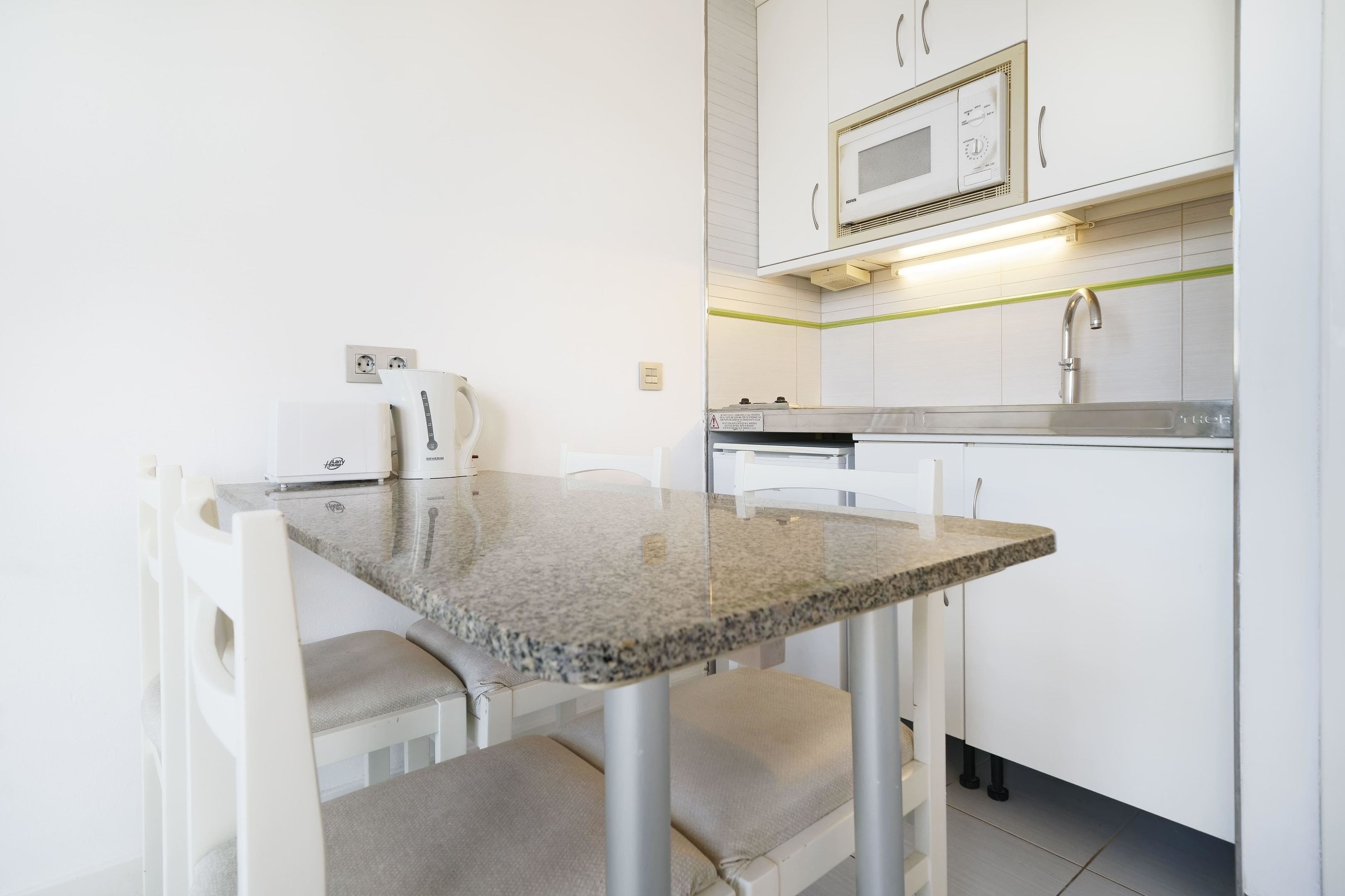 A compact kitchen with white cabinets, a microwave, a kettle, and a granite countertop.