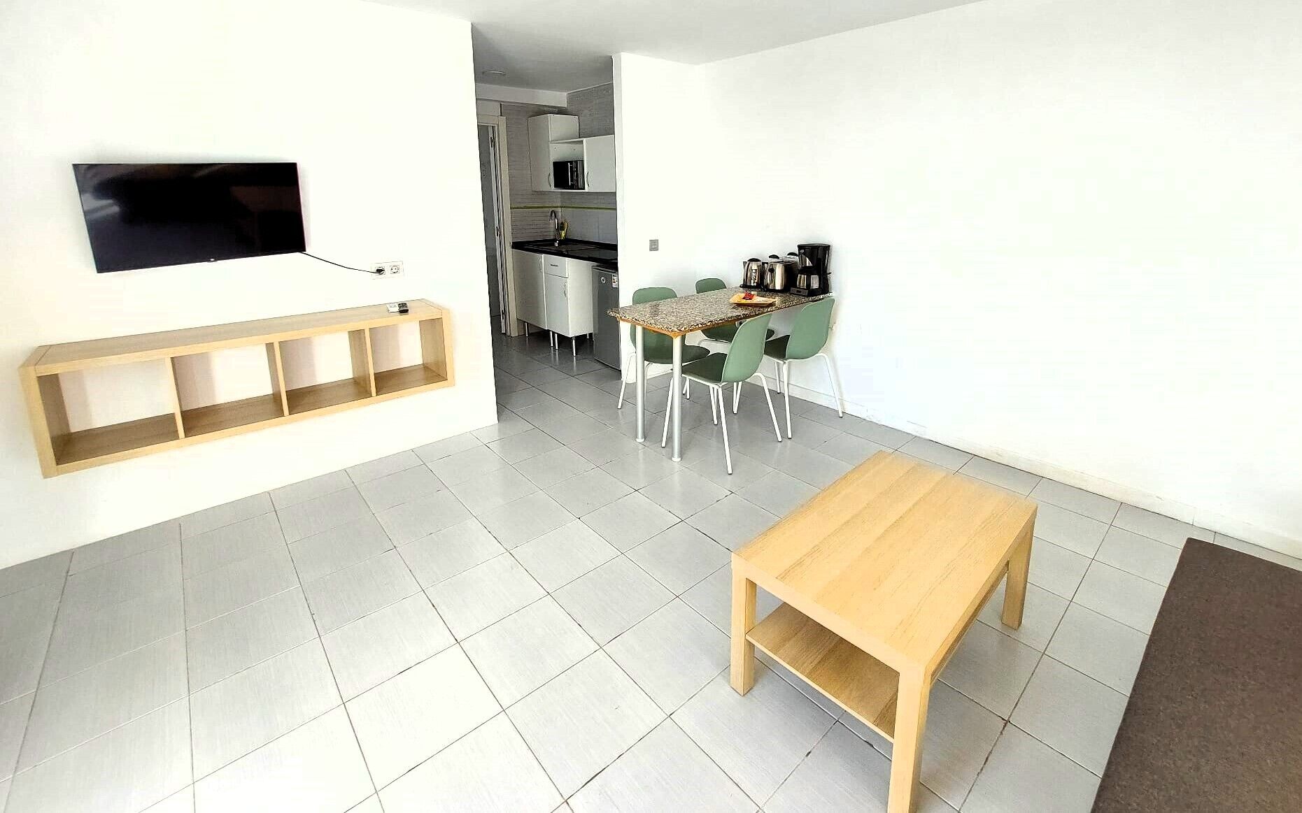 A modern kitchen with a dining area, a TV mounted on the wall, and a wooden bench.