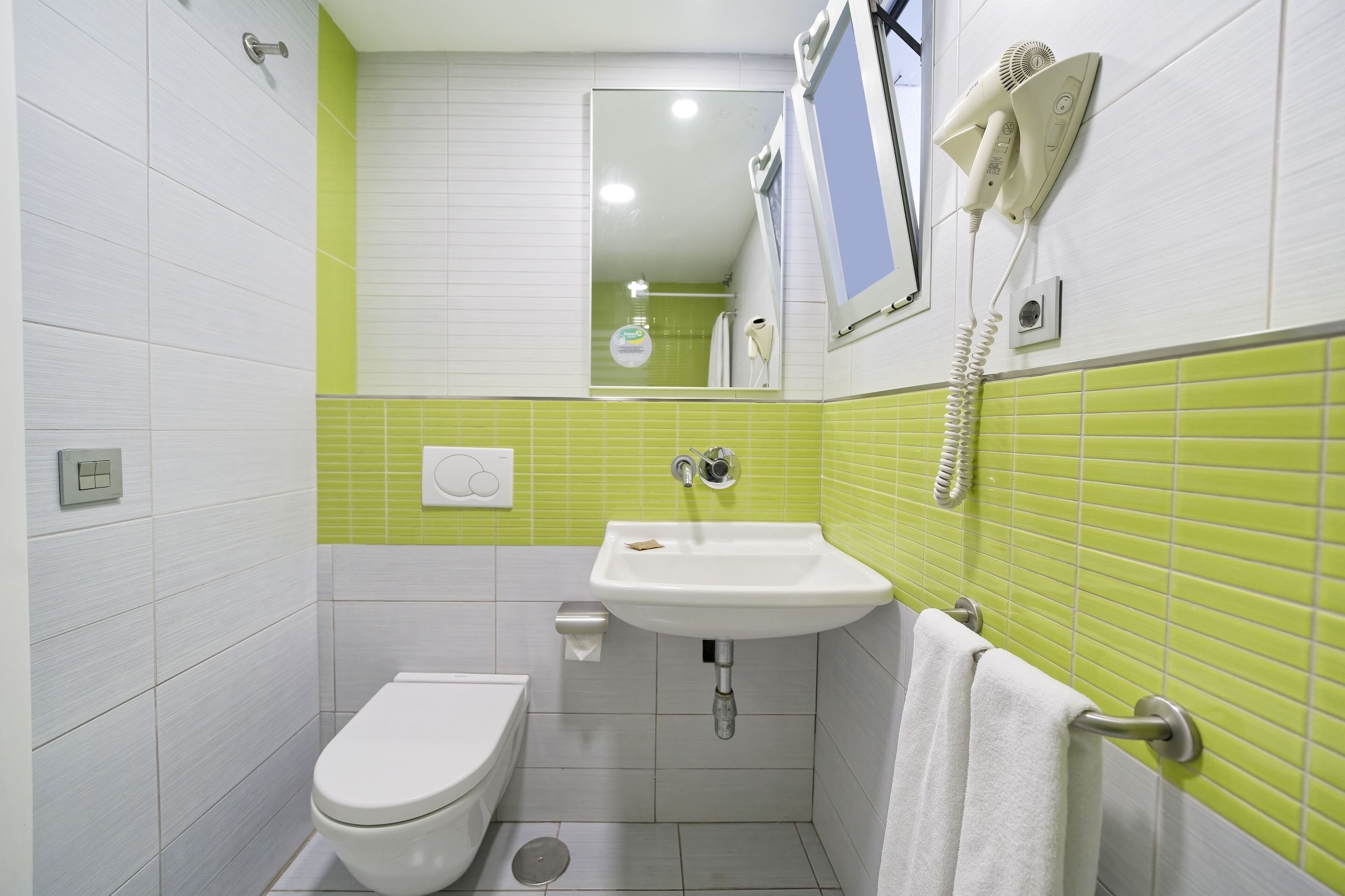 A bathroom with a white toilet, a sink with a mirror above it, and a hairdryer mounted on the wall.