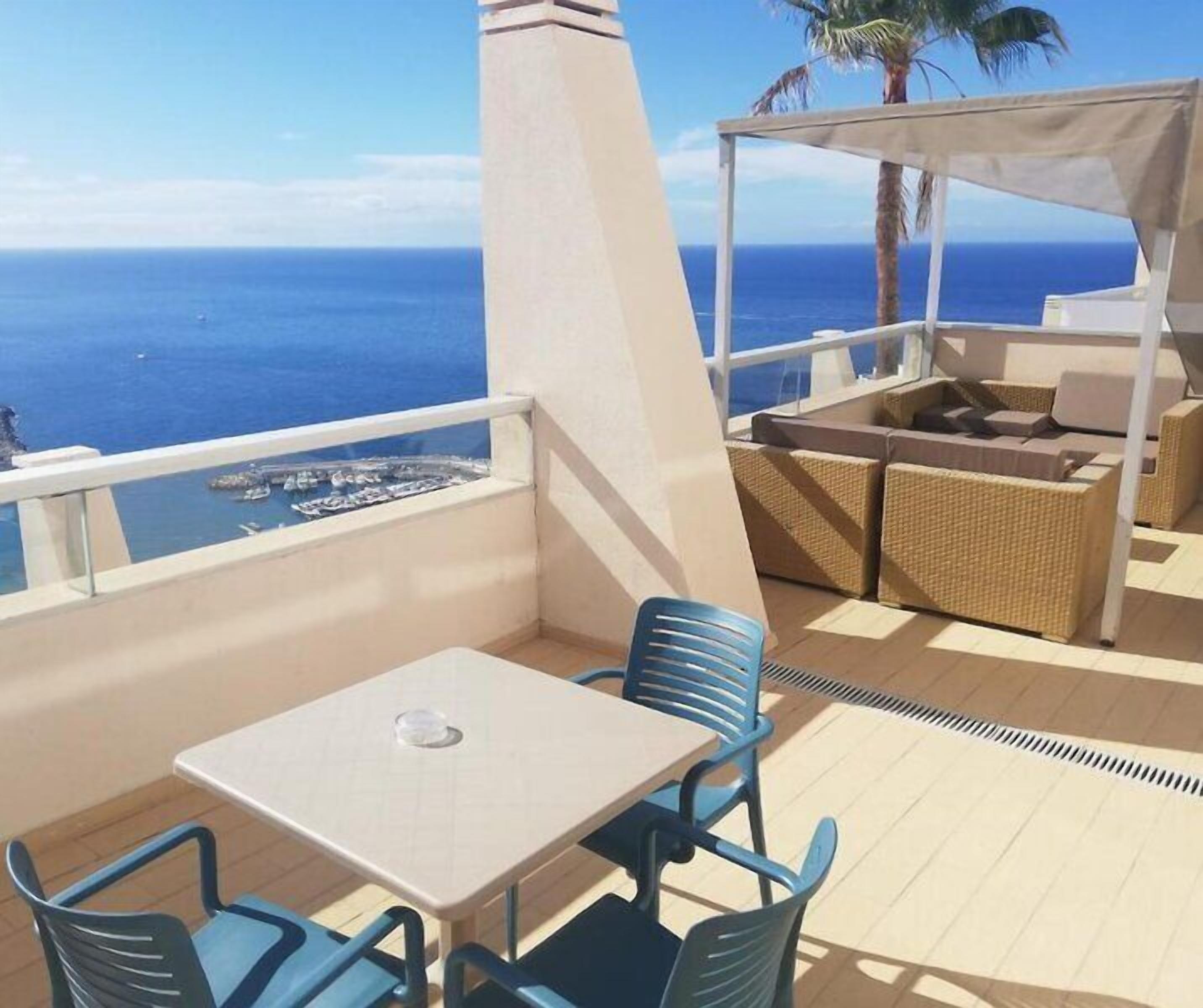 Un balcón con mesa y sillas, vistas al mar y una zona de estar techada.
