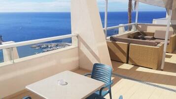 Un balcón con mesa y sillas, vistas al mar y una zona de estar techada.