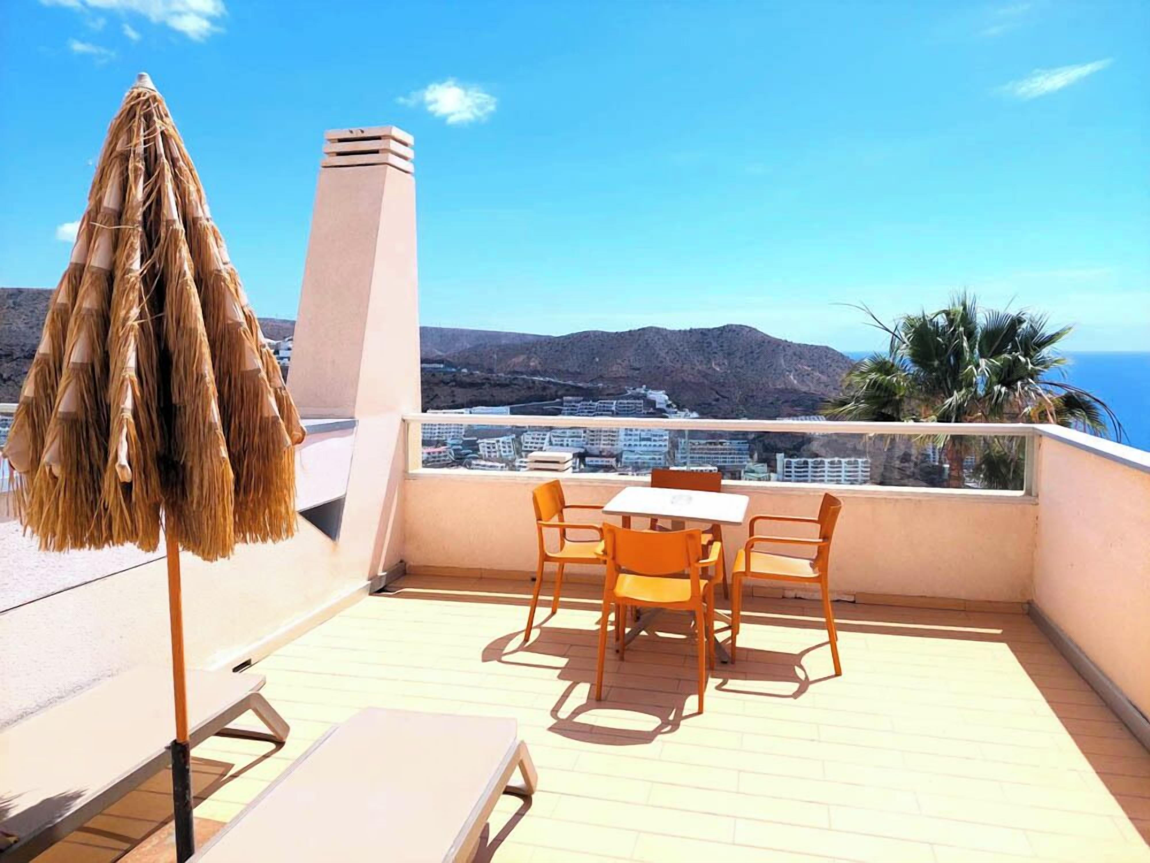 Un balcon avec une table et des chaises, un parasol et une vue sur la mer et les bâtiments.