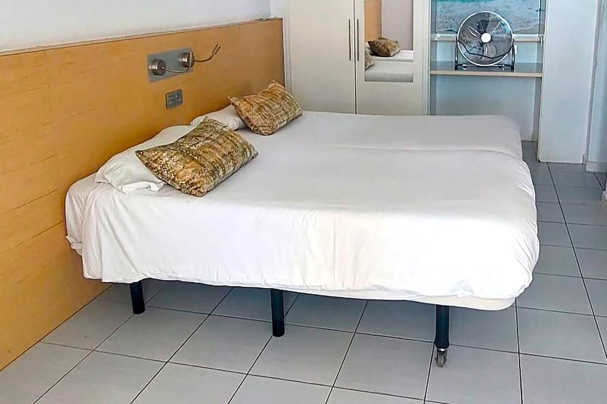 Une chambre d’hôtel avec un lit, une table de chevet, une fenêtre donnant sur l’océan et un ventilateur de plafond.