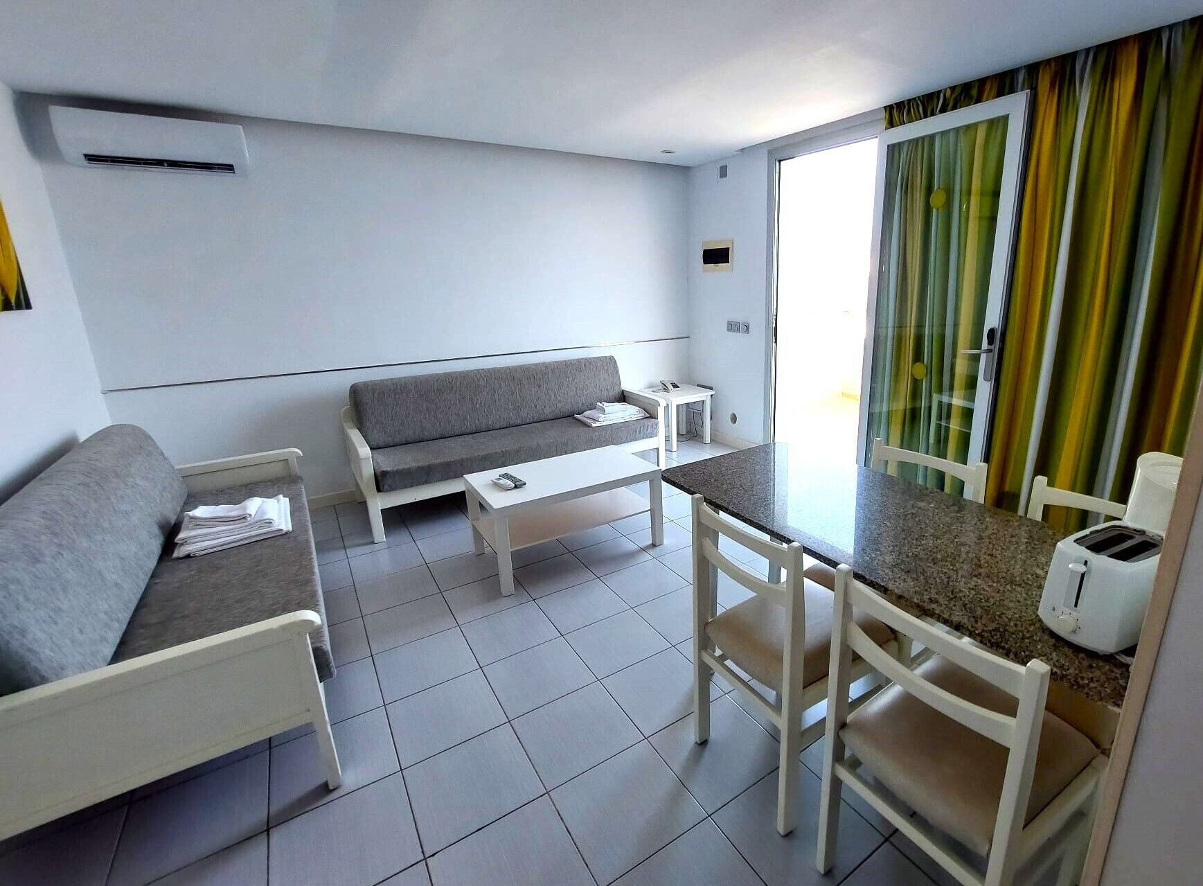 A modern living room with a grey sofa, a white coffee table, and a dining area with a white table and chairs.