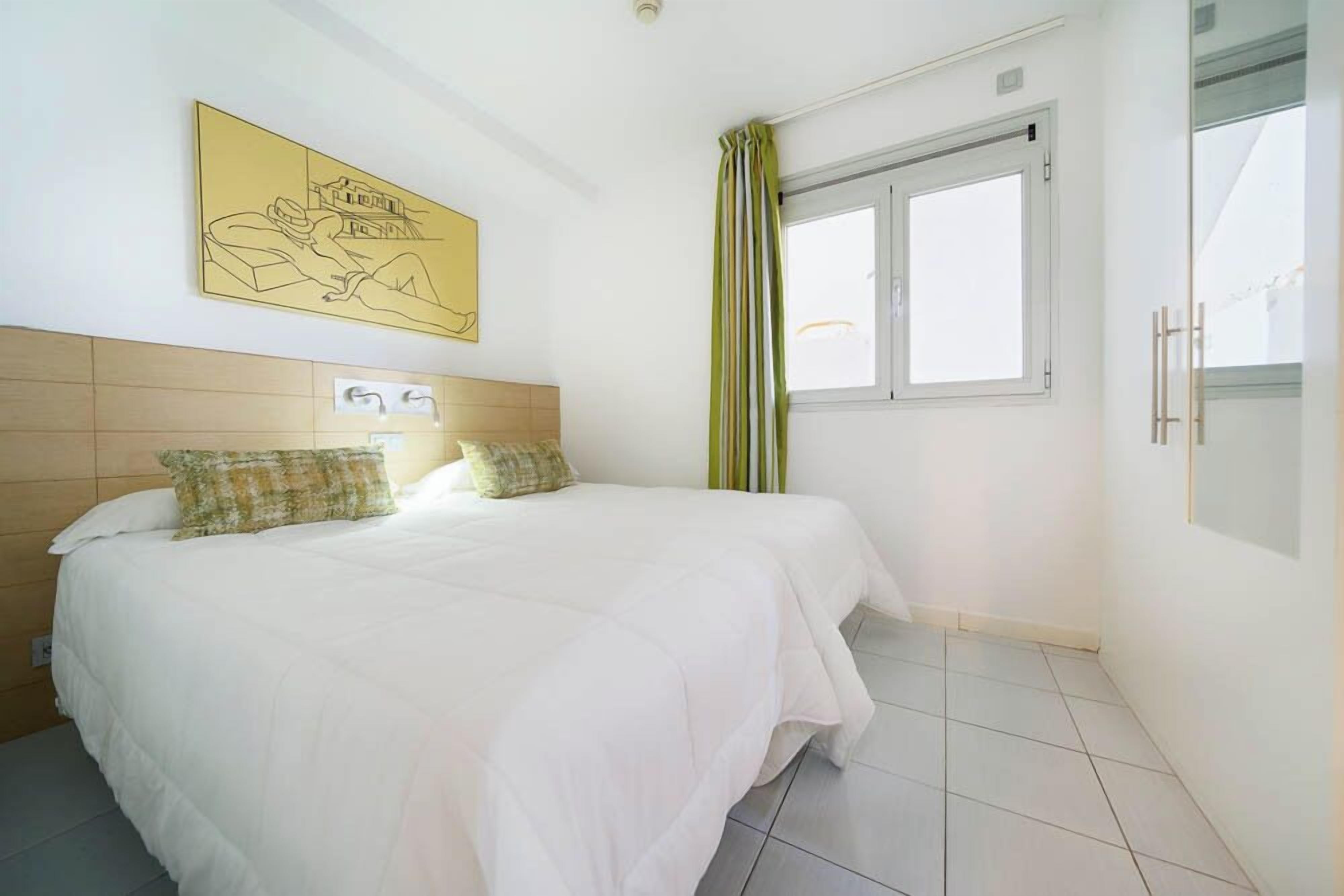 Un dormitorio con cama, ventana y una obra de arte colgada en la pared.