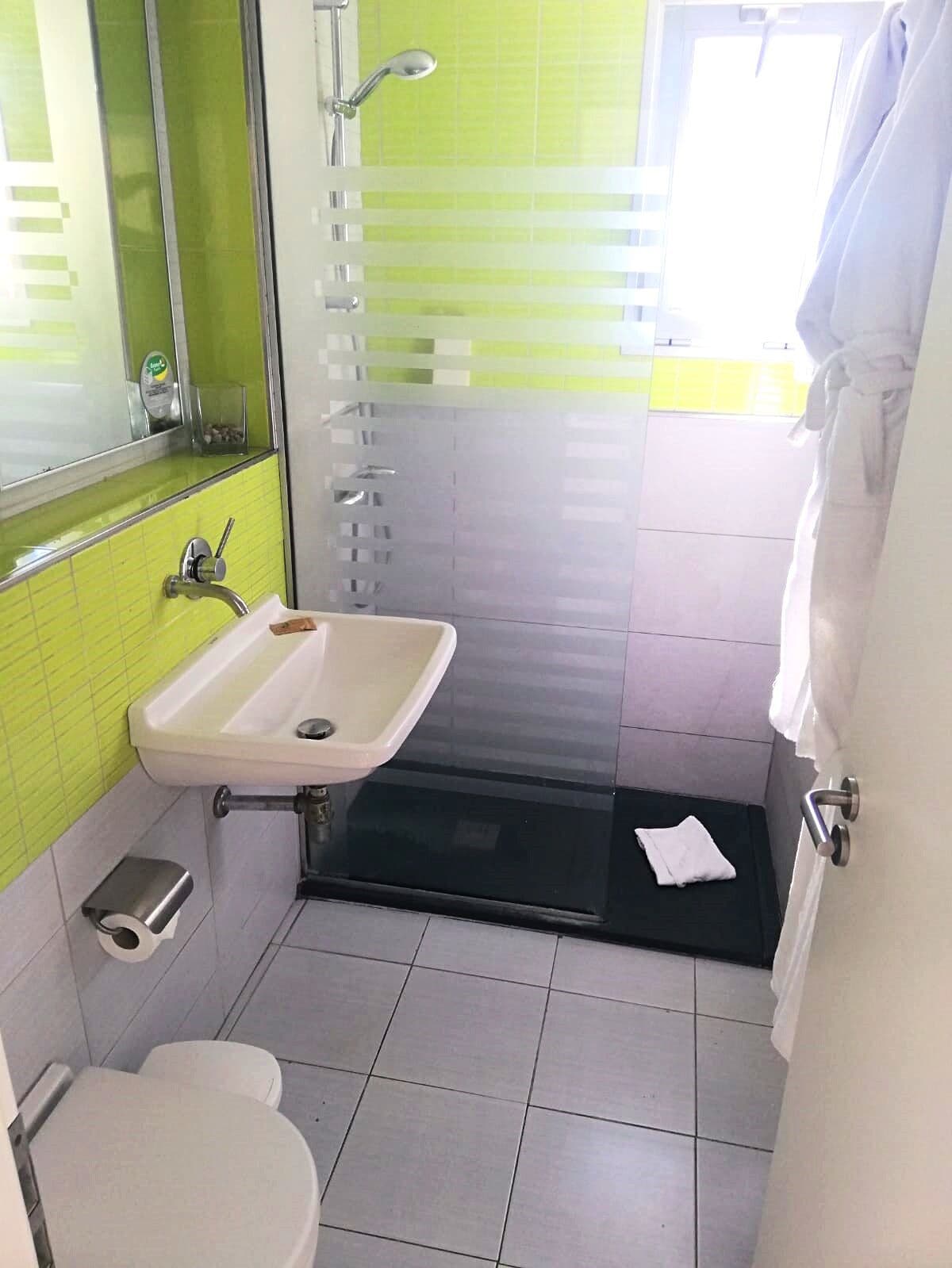 Ein Badezimmer mit weißem Waschbecken, Toilette und einer Duschkabine aus Glas.
