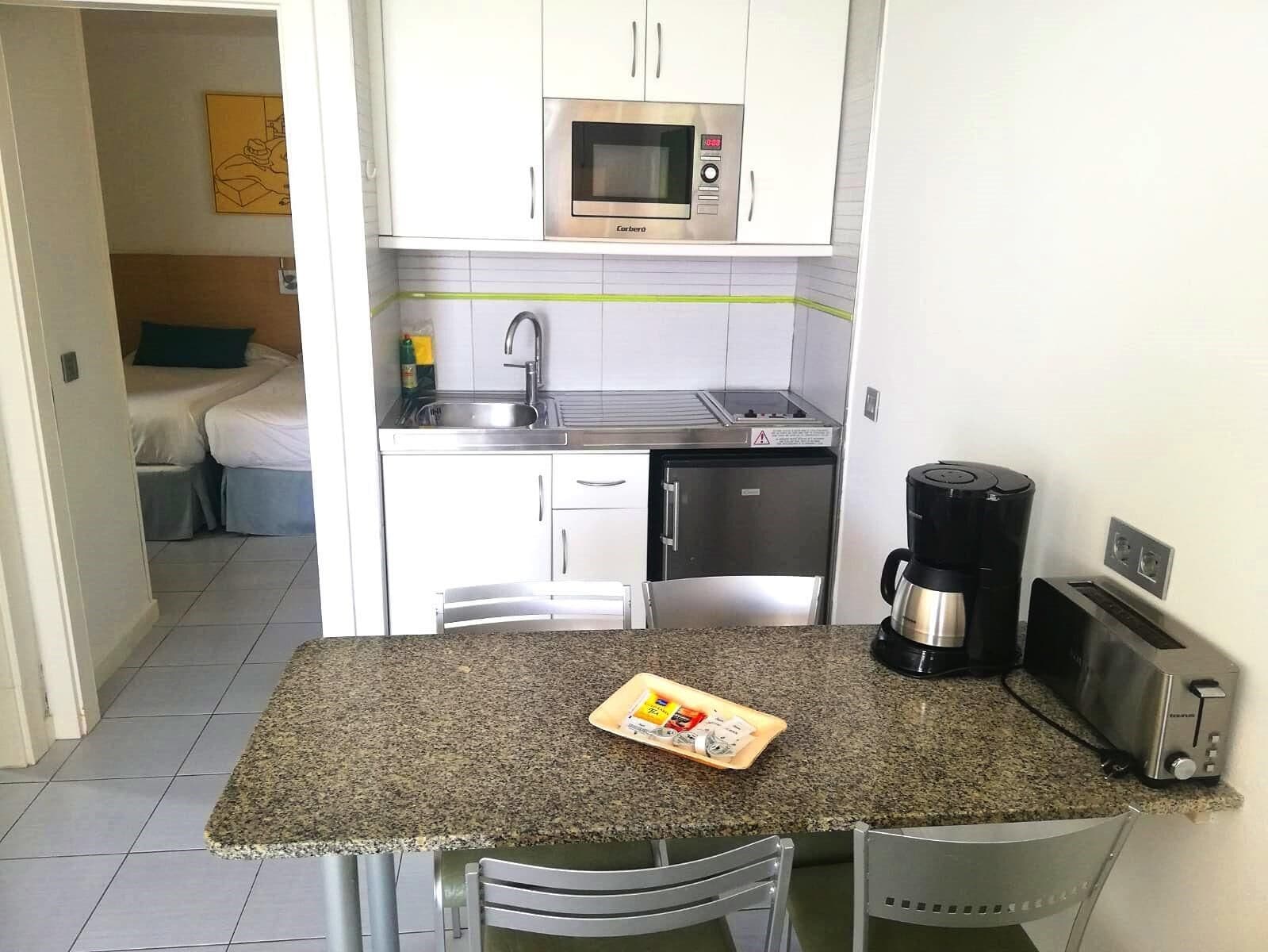A compact kitchenette with a microwave, sink, coffee maker, and toaster.