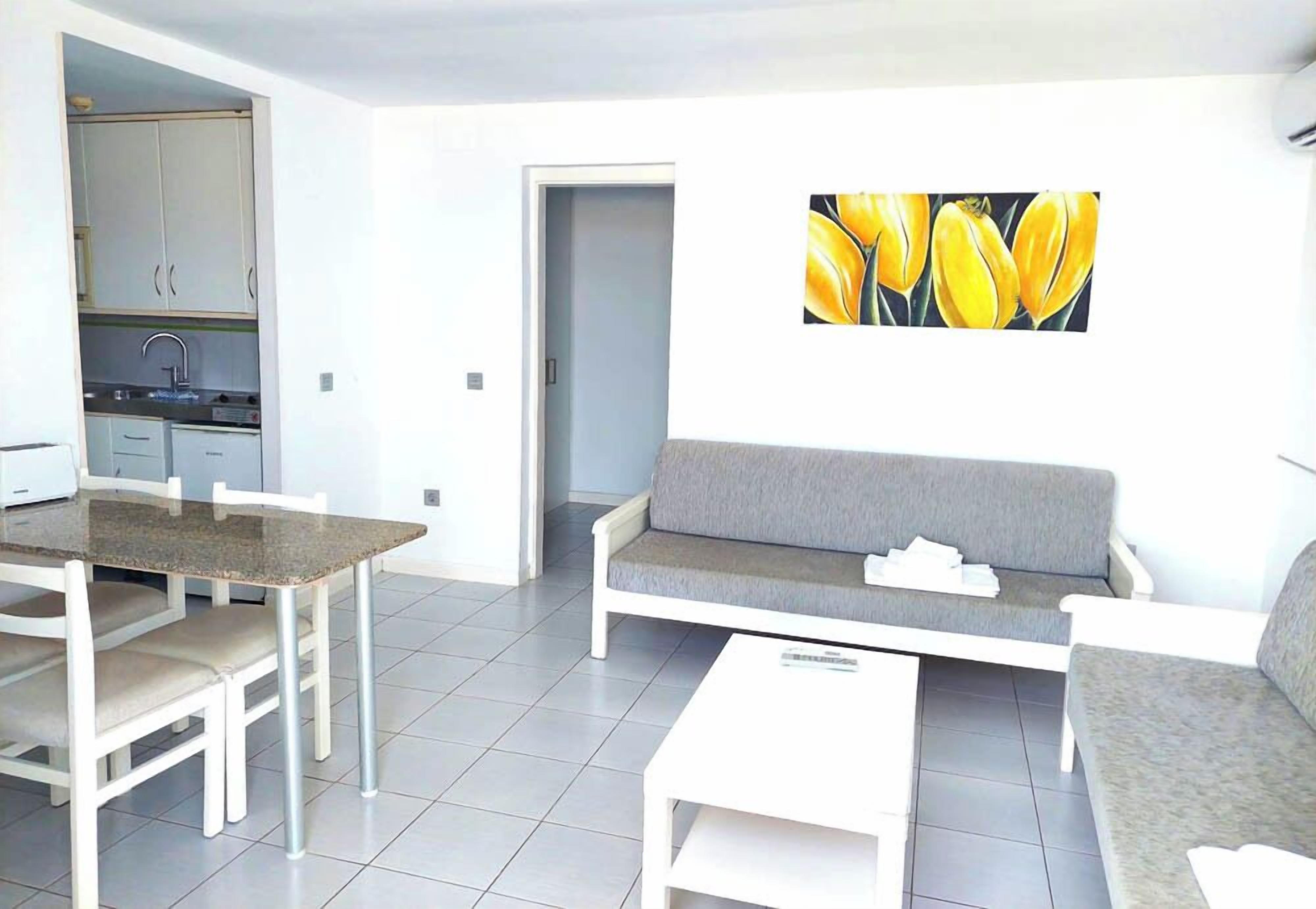 A modern living room with a grey sofa, a dining table with chairs, and a kitchen area with cabinets and a sink.