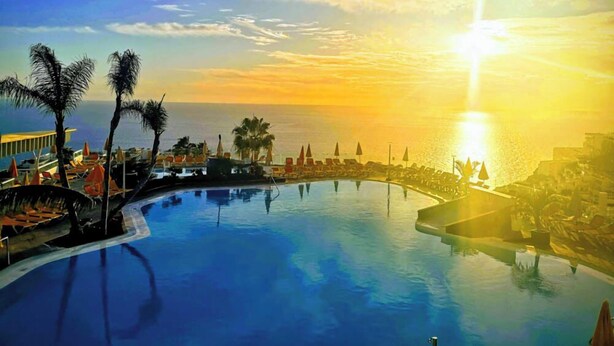 Poolområde i et resort med udsigt til solnedgang, palmer og liggestole.