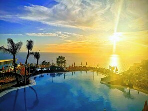 A resort pool with a sunset view, palm trees, and sun loungers. - Servatur Riosol (Mogan)