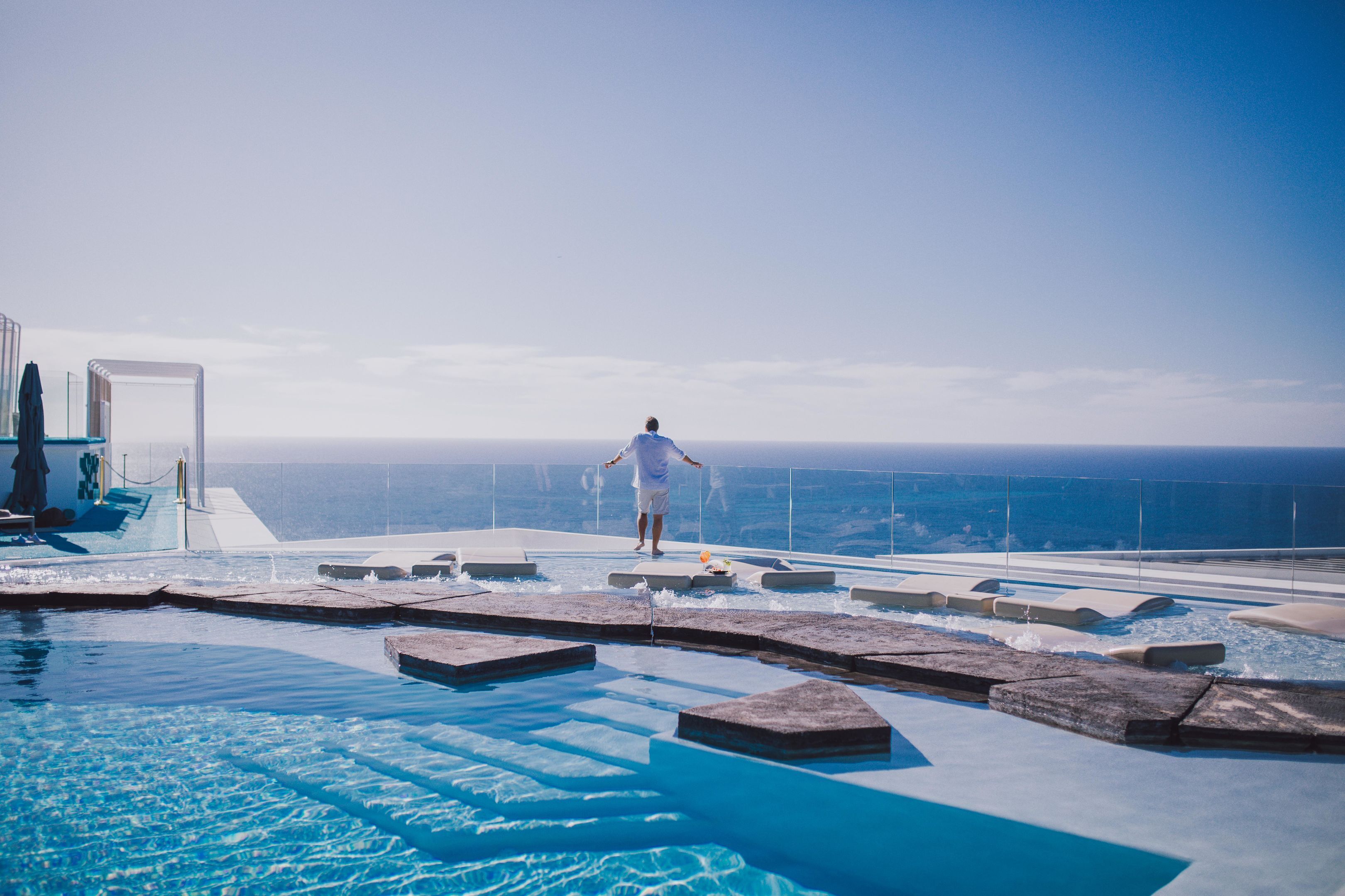 A man walking on a infinity pool deck with a view of the ocean.