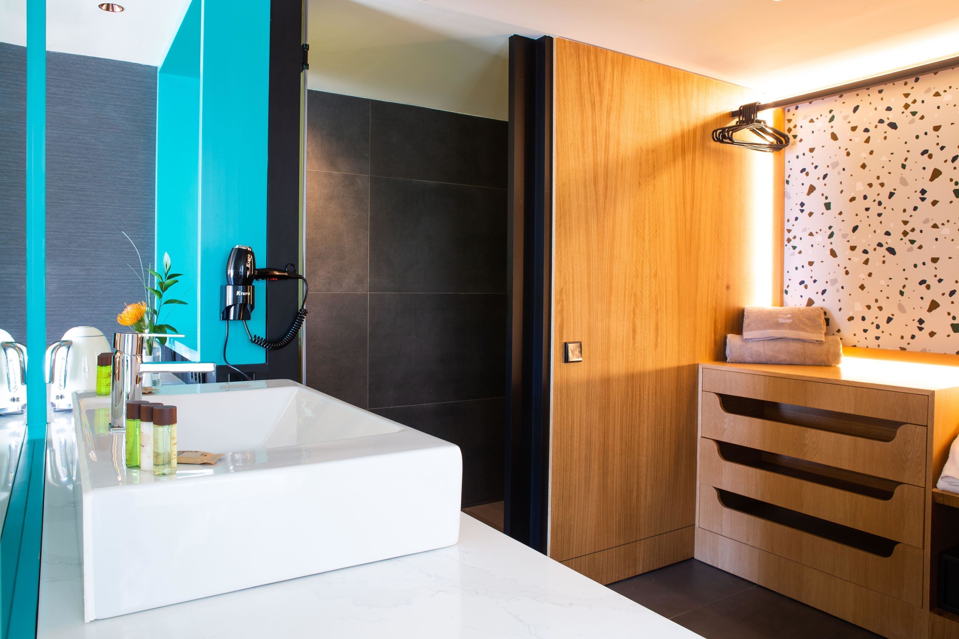 A modern bathroom with a white sink, dark tiles, a wooden vanity, and a towel rack.
