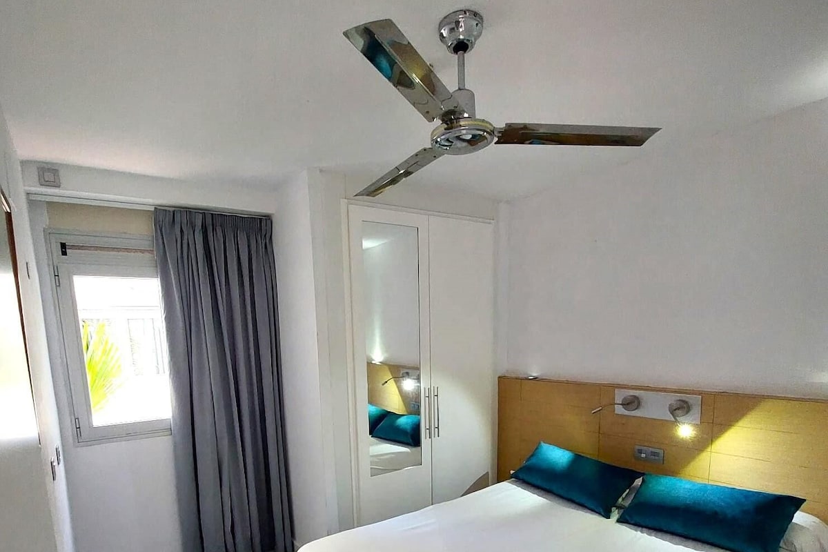 Une chambre d’hôtel avec un lit, un ventilateur de plafond, une fenêtre avec des rideaux et une porte.