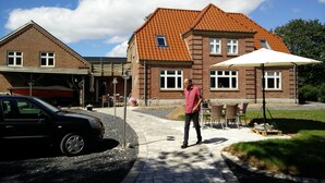 Ein Backsteinhaus mit Ziegeldach, eine überdachte Terrasse mit Gartenmöbeln und ein Auto auf der Auffahrt.