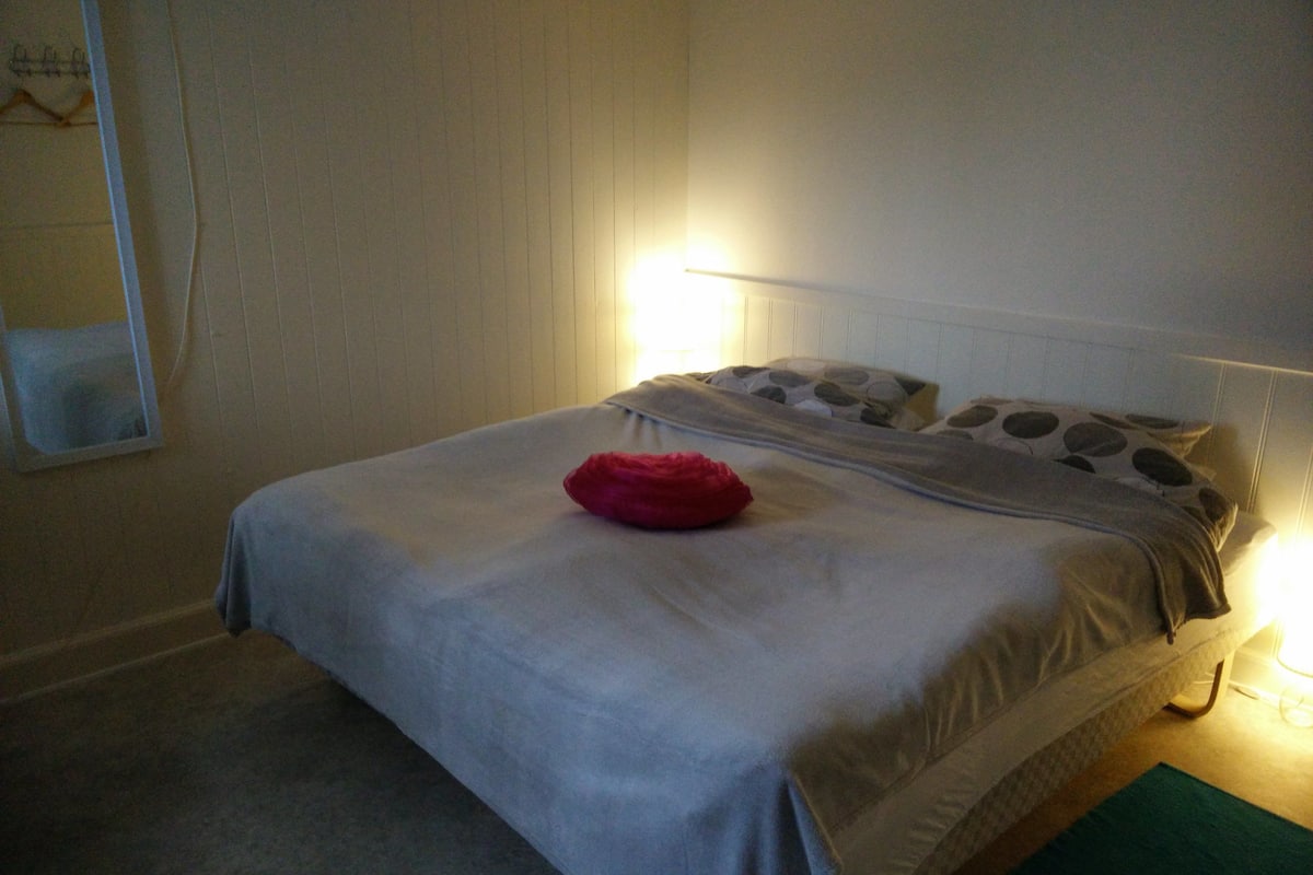 A neatly made bed with a grey bedspread, a red pillow, and patterned pillows.