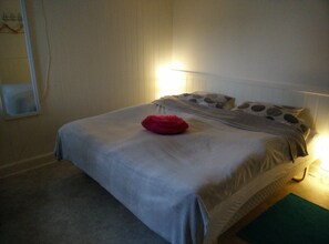 A neatly made bed with a grey bedspread, a red pillow, and patterned pillows.