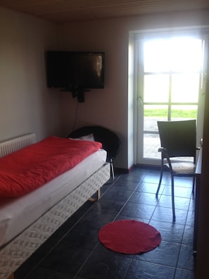 A small room with a bed, a chair, a television, and a door leading outside.