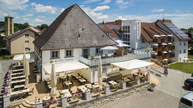 A hotel with a prominent triangular roof, outdoor seating area with umbrellas, and solar panels on the roof. - Bodensee-Hotel Kreuz (Uhldingen-Muehlhofen)