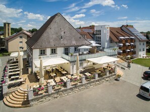A hotel with a prominent triangular roof, outdoor seating area with umbrellas, and solar panels on the roof. - Bodensee-Hotel Kreuz (Uhldingen-Muehlhofen)