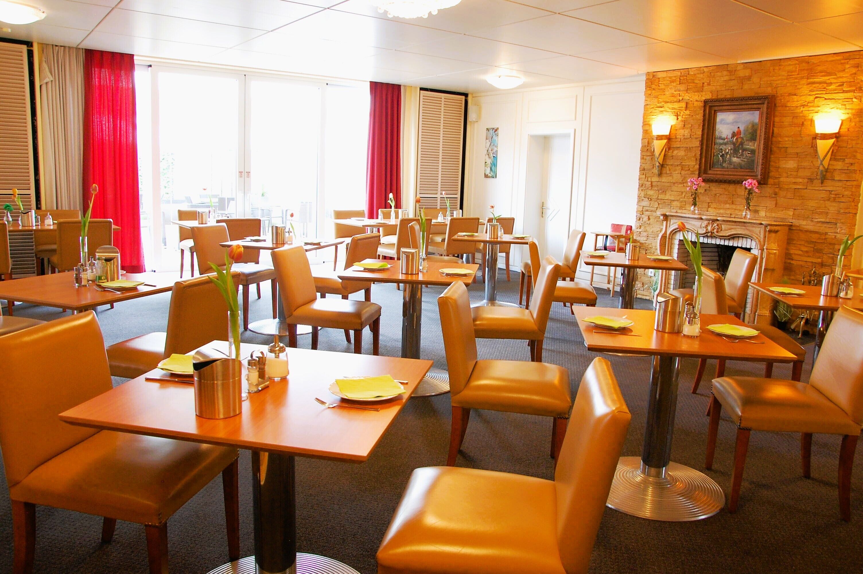 Comedor de hotel con varias mesas y sillas, una chimenea y vistas al exterior a través de grandes ventanales.