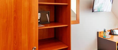 Una habitación con un armario de madera, un escritorio con una computadora, un cesto de basura y un televisor montado en la pared.