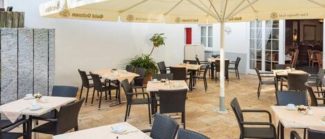 An outdoor dining area with tables and chairs, covered by umbrellas, and a sign reading "Gold Ochsen".
