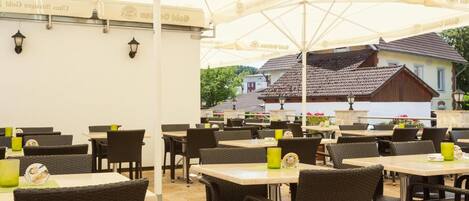 An outdoor dining area with tables and chairs, umbrellas, and a view of a building in the background.