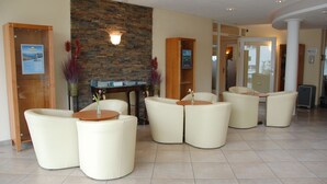 A lobby with a stone wall, a reception desk, and several seating areas with round tables. - Bodensee-Hotel Kreuz (Uhldingen-Muehlhofen)
