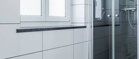 A modern bathroom with a glass shower enclosure, a window, and a tiled floor.