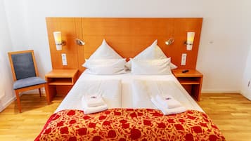 A double bed with a wooden headboard, two bedside tables, a chair, and a red floral bedspread.