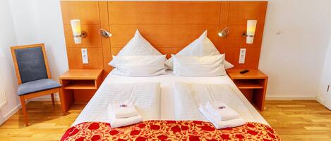 A double bed with a wooden headboard, two bedside tables, a chair, and a red floral bedspread.