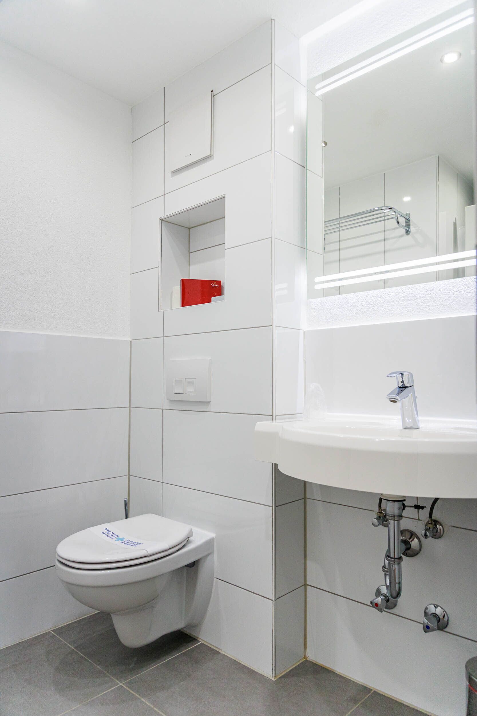 Un baño moderno con un inodoro blanco, un lavabo con un espejo encima y un objeto rojo en la pared.