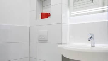 Un baño moderno con un inodoro blanco, un lavabo con un espejo encima y un objeto rojo en la pared.