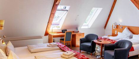 A cozy room with a bed, two chairs, a desk, and a small table.