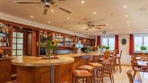 A bar area with wooden stools, a counter, and a variety of bottles and glasses. - Bodensee-Hotel Kreuz (Uhldingen-Muehlhofen)