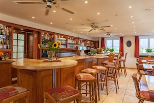 Una zona de bar con taburetes de madera, una barra y una variedad de botellas y vasos.