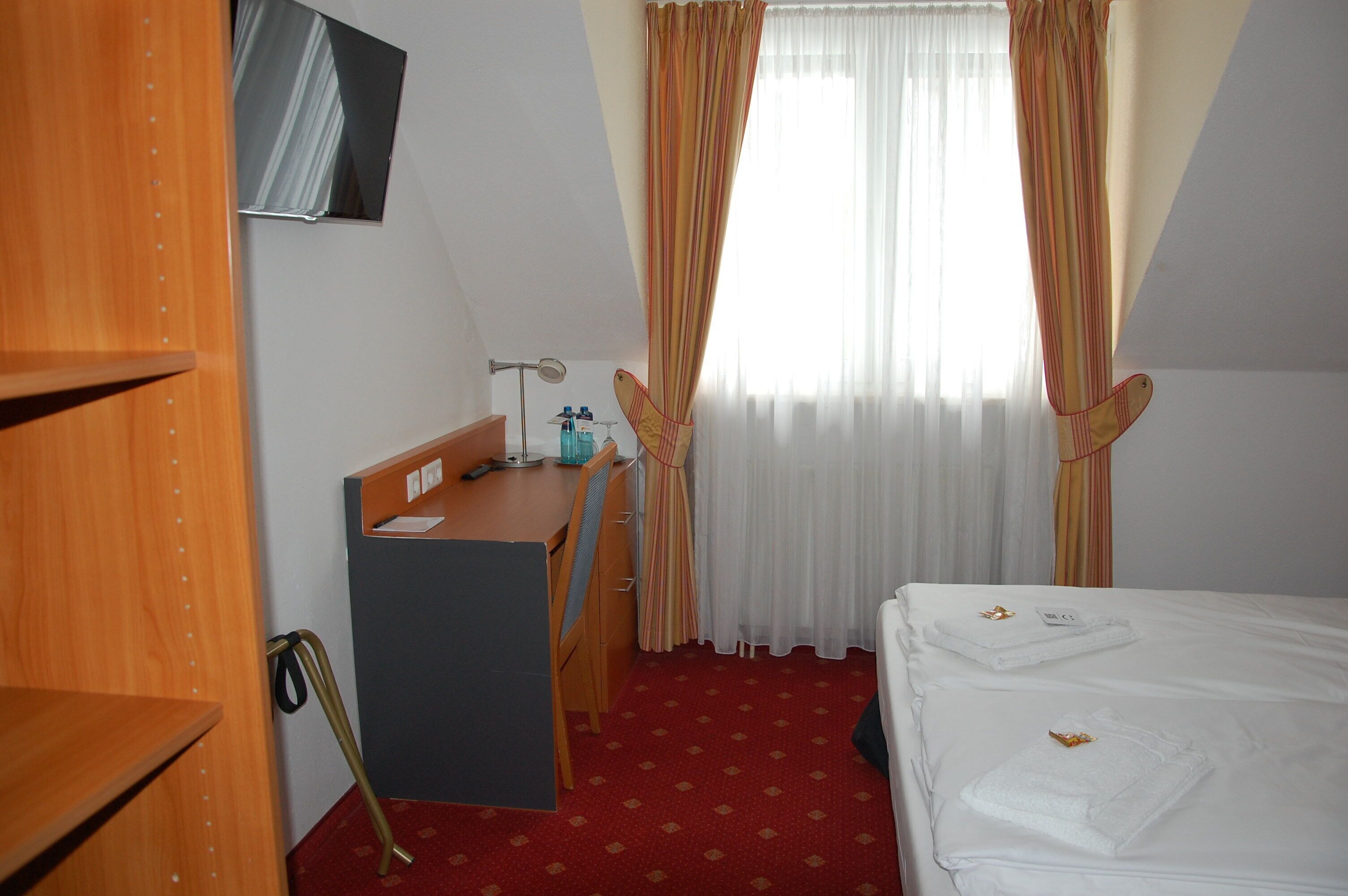 A hotel room with a desk, chair, bed, and a TV mounted on the wall.