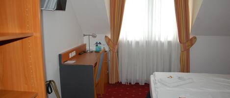 A hotel room with a desk, chair, bed, and a TV mounted on the wall.