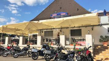 A row of motorcycles parked outside a building with a tiled roof and a covered outdoor seating area.