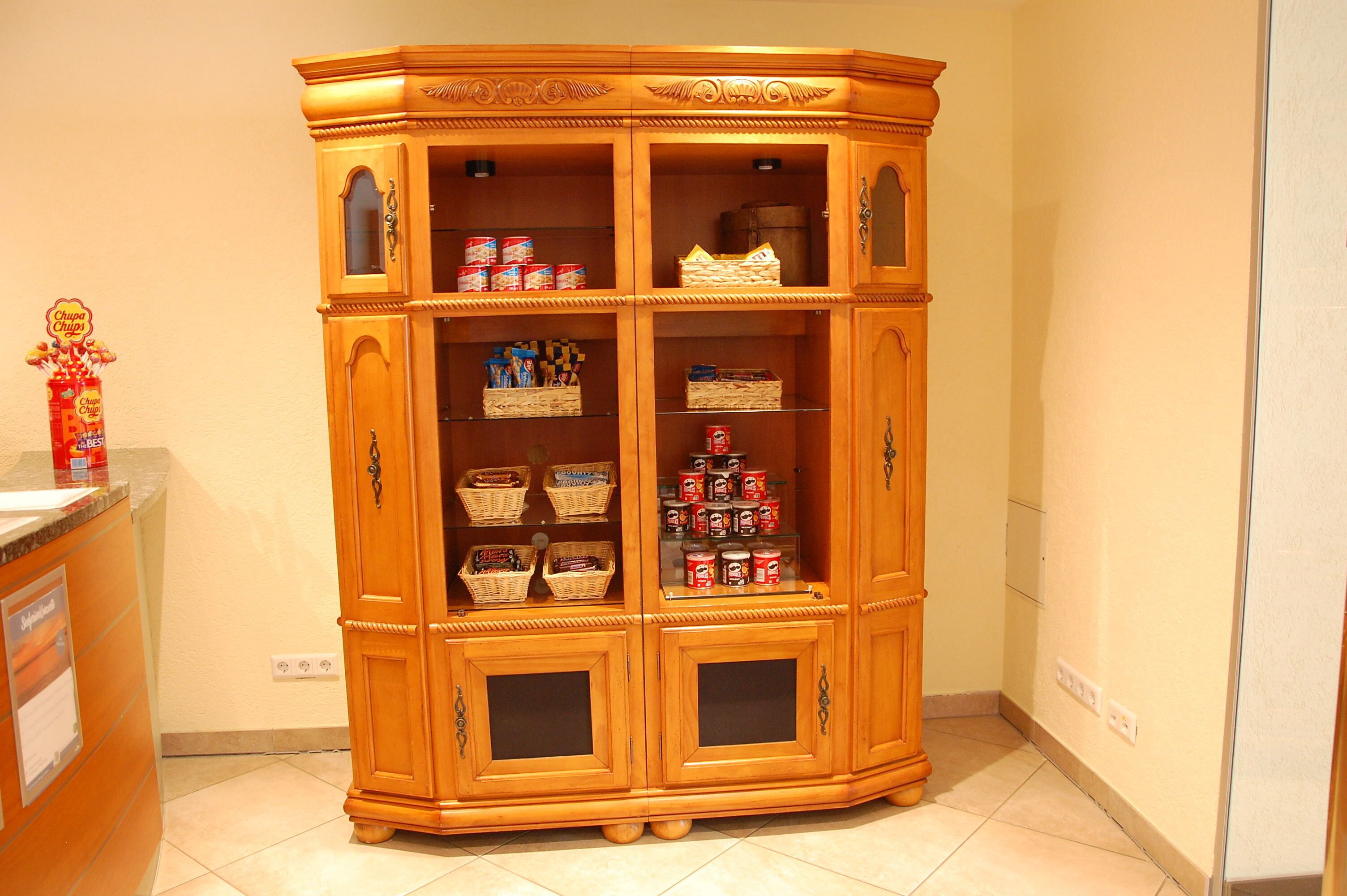 A wooden double-door cabinet with multiple shelves and drawers, containing various items like baskets and canned goods.