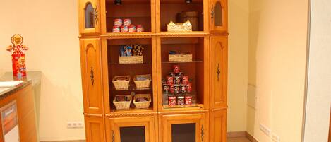 A wooden double-door cabinet with multiple shelves and drawers, containing various items like baskets and canned goods.